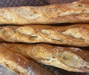 4 Baguete Italiana Crosta Parmesão sobre uma mesa de madeira e grade de aço da Padaria Artesanal Delivery Conexão Delícia