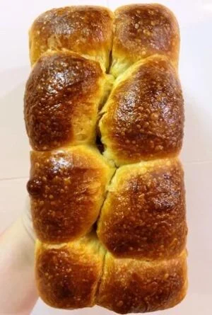 Um Pão Brioche de Fermentação Natural a Padaria Artesanal Conexão Delícia seguro por uma mão