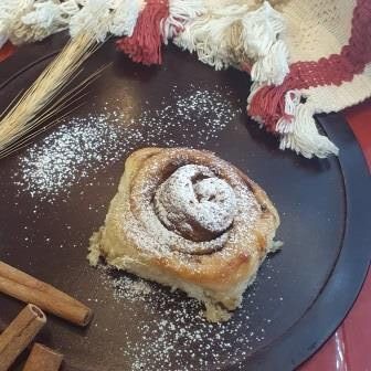 Cinnamon Roll sobre uma tábua de pães com pedaços de canela um ramo de trigo e uma toalha