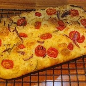 Focaccia Tomate Cereja de Fermentação natural da Padaria Artesanal Conexão Delícia sobre uma tela de metal preto que está sobre uma mesa