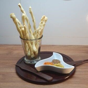 Grissini Azeite e Ervas Finas Grissini Azeite e Ervas Finas em um copo sobre uma mesa de madeira ao lado de um prato com antepasto. da Padaria Artesanal Delivery Conexão Delícia